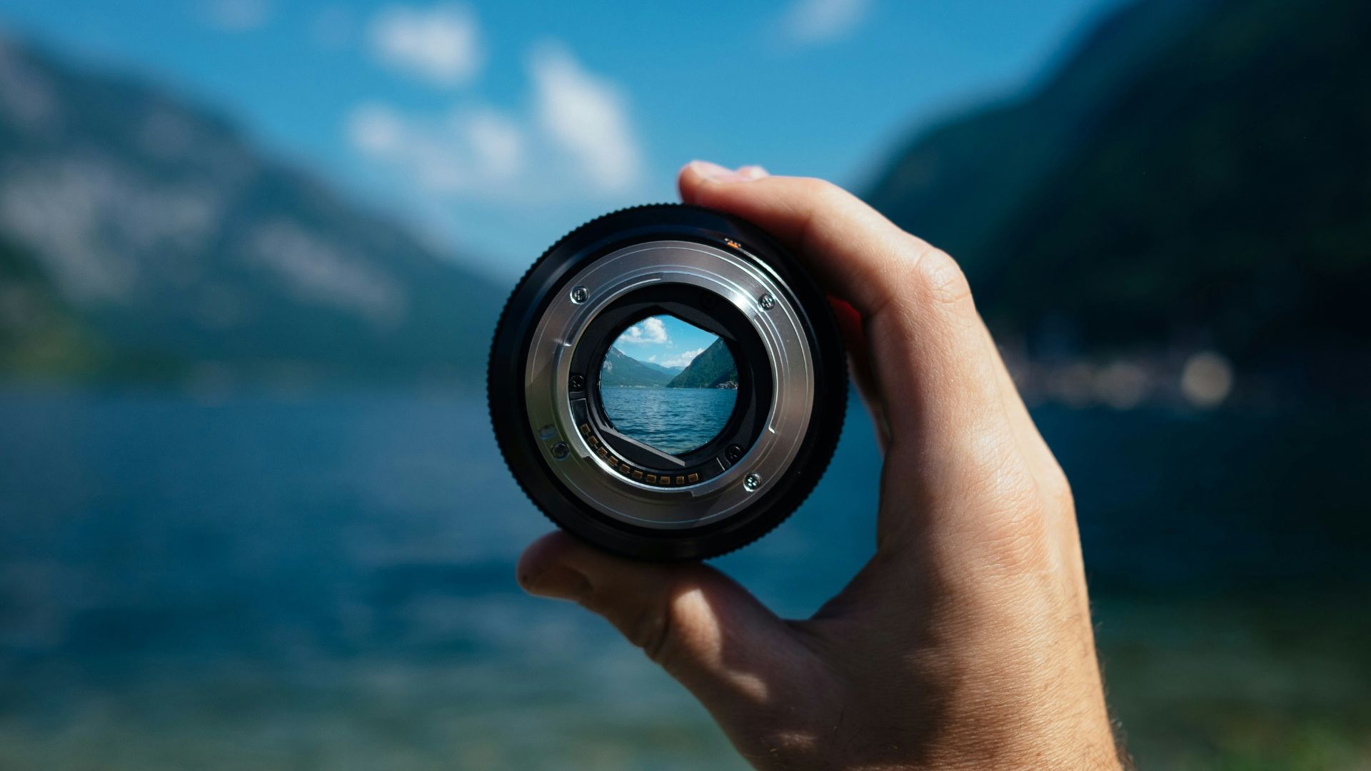 Hand holding camera lense up to blurry mountain lake landscape